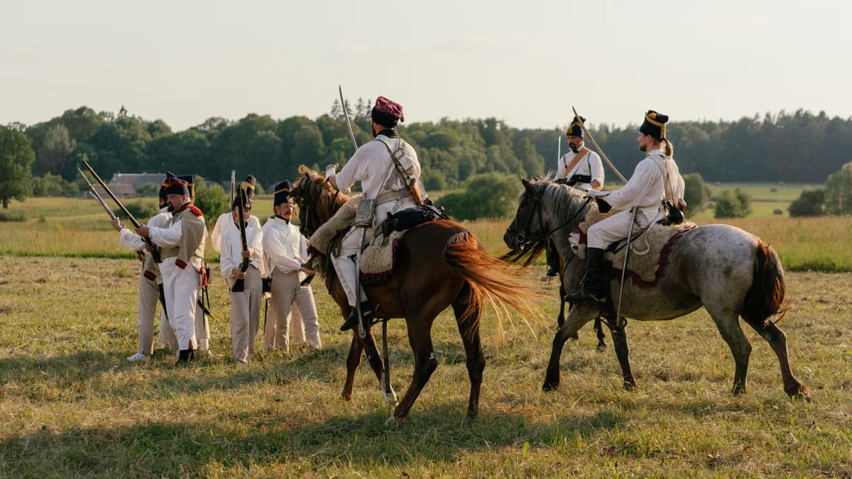 Reenactment of historical military horseback and infantry in outdoor setting.